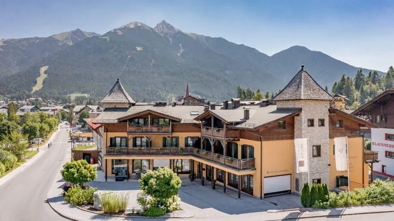 Modernes Gebäude im alpinen Stil mit Balkonen und beeindruckendem Bergblick unter blauem Himmel.