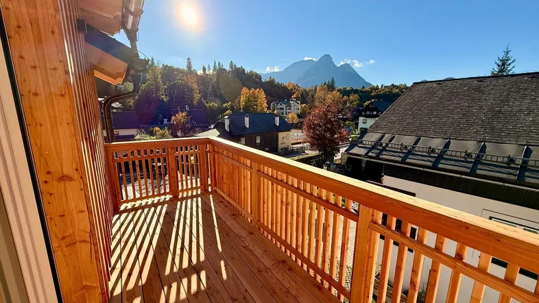 Sonnige Holzterrasse mit Bergblick und traditionellem Geländer, ideal zum Entspannen im Freien.