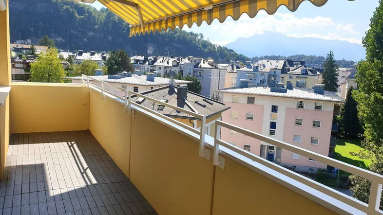 Geräumiger Balkon mit gestreifter Markise, Holzboden und weitem Blick auf die Stadt und Berge.