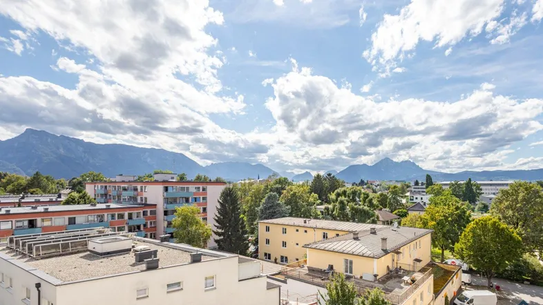 Weitläufiger Blick über die Stadt mit umliegenden Gebäuden, viel Grün und beeindruckendem Bergpanorama.