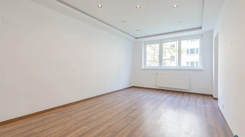 Heller, unmöblierter Raum mit Laminatboden, großen Fenstern und integrierten Deckenleuchten.