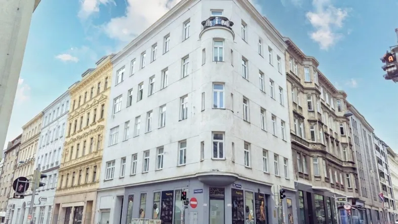 Klassisches Eckgebäude in urbaner Umgebung mit kleinen Balkonen und vielen Fenstern.
