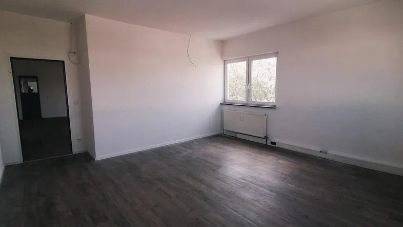 Helles, leeres Zimmer mit Laminatboden und einem Fenster, bereit zur individuellen Gestaltung.