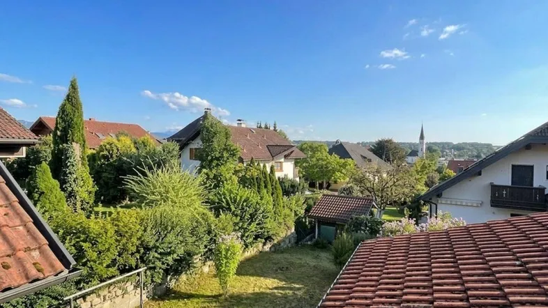 Blick über die Dächer der Nachbarschaft mit grünen Gärten und einem Kirchturm in der Ferne.