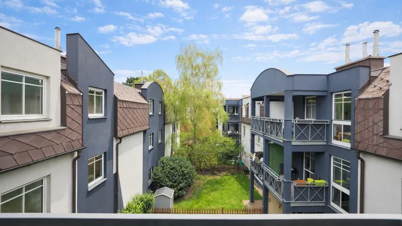 Blick von einem Balkon in einen begrünten Innenhof zwischen modernen Wohngebäuden.