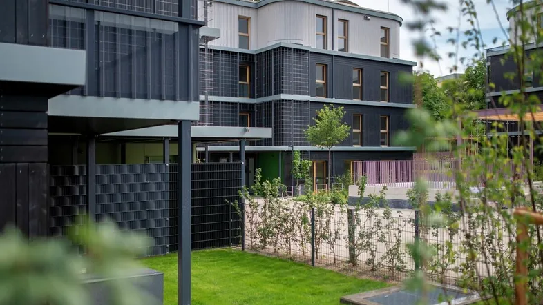 Moderner Gebäudekomplex mit dunkler Fassade, Balkonen und gepflegter Grünfläche im Vordergrund.