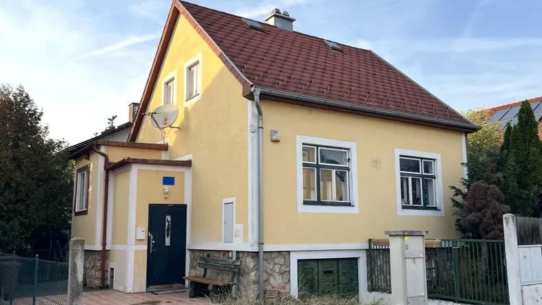 Gelbes Einfamilienhaus mit rotem Ziegeldach und Vorgarten in sonniger Lage.