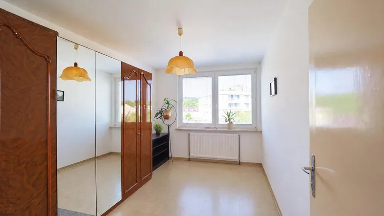 Helles Schlafzimmer mit großem Spiegelschrank, Fliesenboden und Blick ins Grüne.