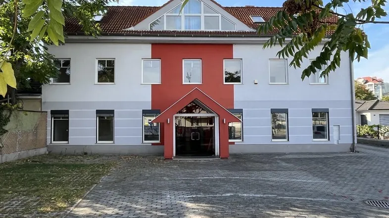 Vorderansicht eines modernen Gebäudes mit rotem Eingangsbereich und großen Fenstern.