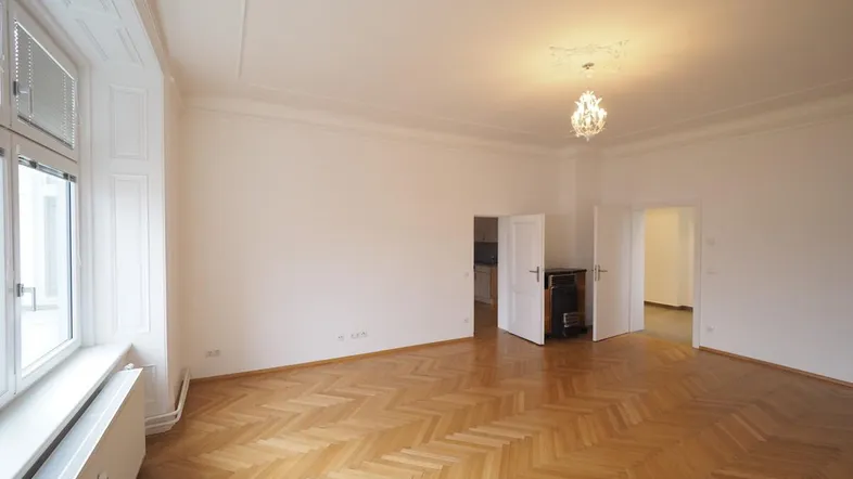 Helles Wohnzimmer mit Fischgrätparkett, hohen Decken und Stuckverzierungen an der Decke.