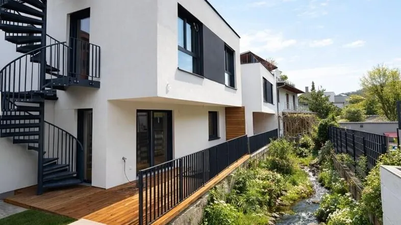 Moderne Architektur mit Außentreppe, Holzterrasse und einem kleinen Bachlauf im Garten.