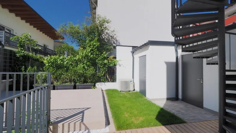 Außenbereich mit Holzterrasse, Rasenfläche und Wendeltreppe zum oberen Stockwerk.