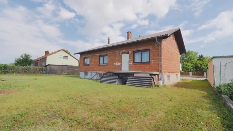 Einfamilienhaus im Rohbau mit großem Garten und Blick auf die ländliche Umgebung.