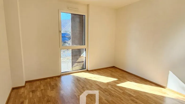 Heller Raum mit Holzboden und großem Fenster, das viel Tageslicht hereinlässt.