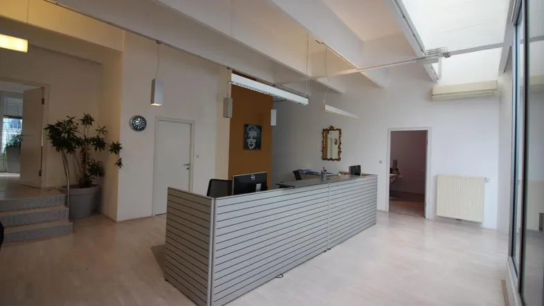 Empfangsbereich eines modernen Büros mit hellem Holzboden, hohen Decken und Oberlichtern für natürliches Licht.