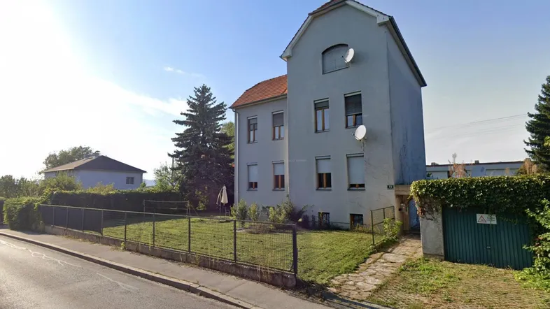 Außenansicht eines Wohnhauses mit Garten und Zaun an einem sonnigen Tag.