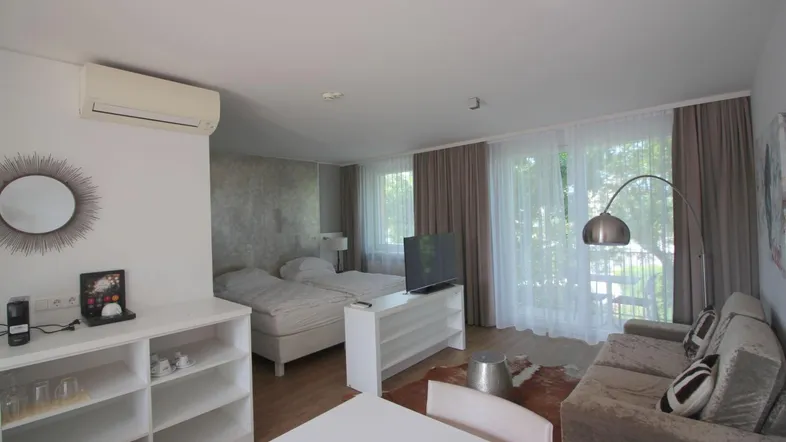 Heller Wohn- und Schlafbereich mit zwei Betten, Sofa, Esstisch und Zugang zum Balkon.