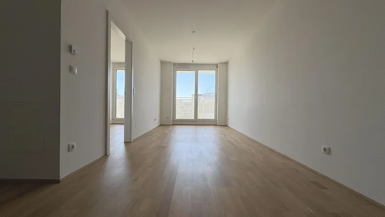 Helles, leeres Zimmer mit Holzboden und Zugang zu einem Balkon, bereit zur individuellen Gestaltung.