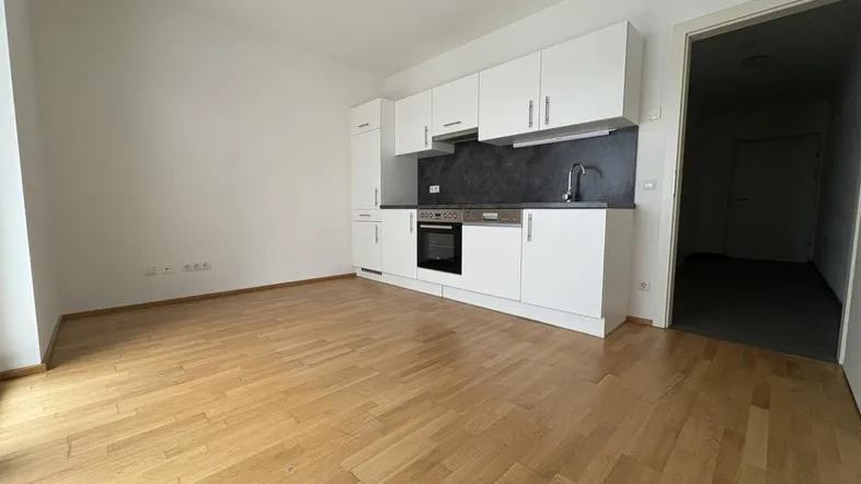 Heller Raum mit integrierter weißer Küchenzeile und warmem Holzparkettboden, ideal für offenes Wohnen.