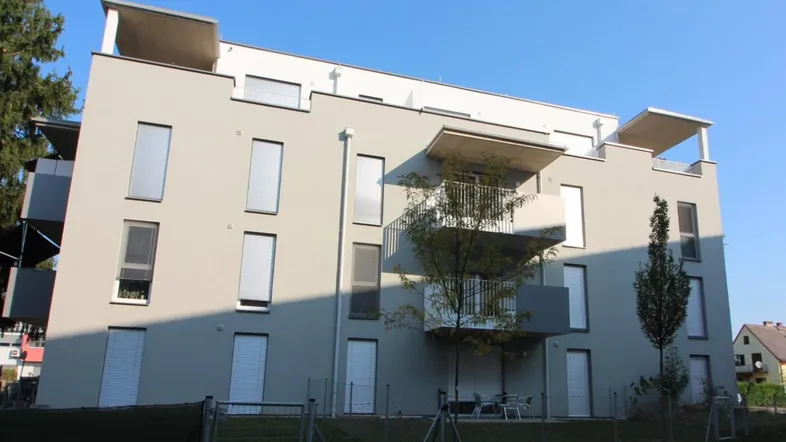 Modernes Mehrfamilienhaus mit heller Fassade, Balkonen und großen Fenstern unter blauem Himmel.