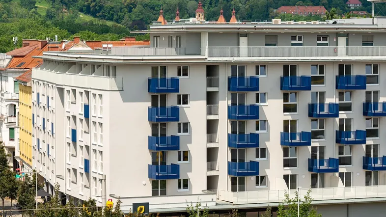 Moderne Wohnanlage mit blauen Balkonen und Blick auf grüne Hügel.