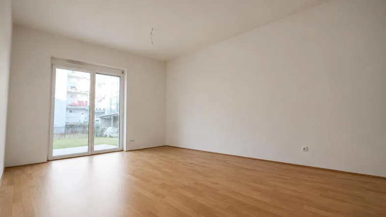 Helles Wohnzimmer mit Parkettboden und Zugang zu einer Grünfläche im Freien.