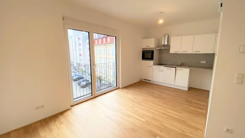 Heller Wohn-Essbereich mit Parkettboden, integrierter Küchenzeile und Zugang zu einem französischen Balkon.