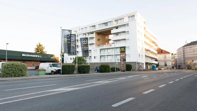 Modernes weißes Gebäude mit Balkonen und großen Fenstern an einer städtischen Straße.