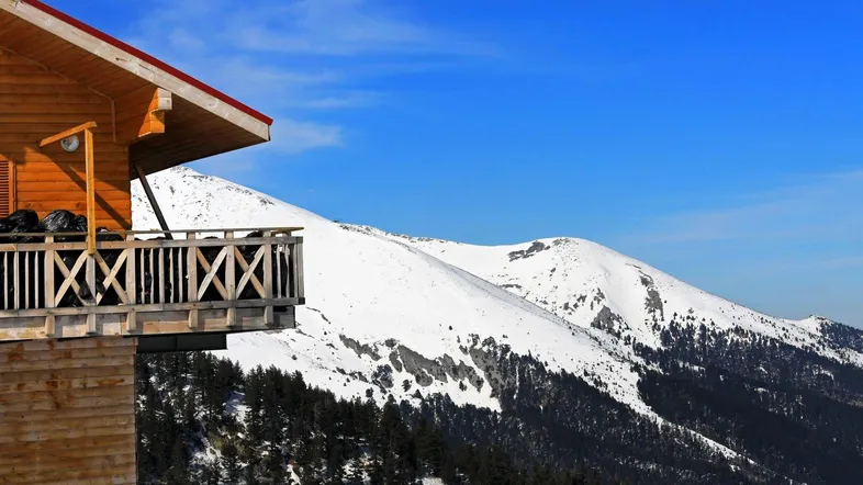 Hölzernes Chalet mit Balkon und atemberaubendem Blick auf schneebedeckte Berge unter blauem Himmel.