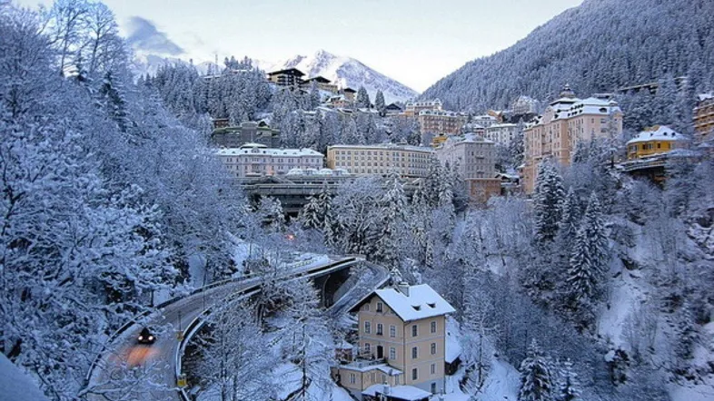 Winterliche Berglandschaft mit verschneiten Gebäuden und Straßen in einem alpinen Tal.