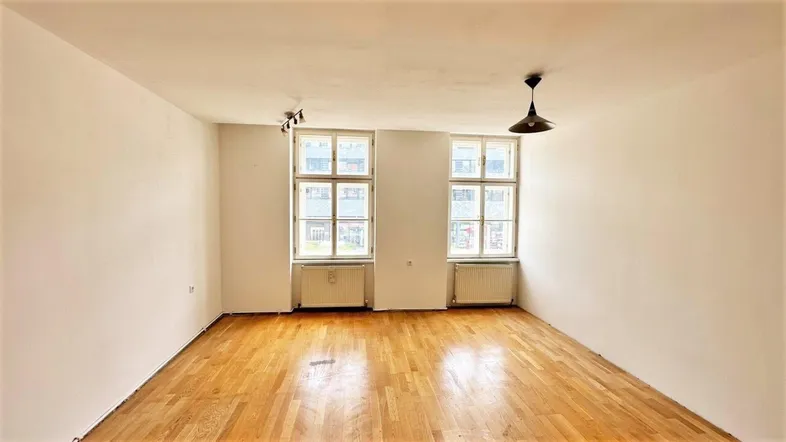 Helles, leeres Wohnzimmer mit Parkettboden und zwei großen Fenstern, bereit zur Einrichtung.