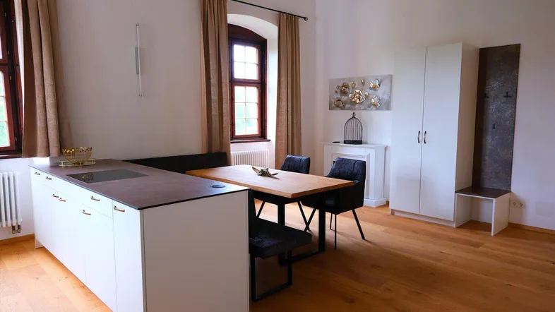 Heller, offener Wohn- und Essbereich mit moderner Einbauküche, Holzboden und hohen Decken.