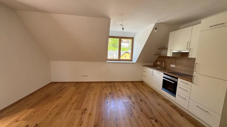 Helle Dachgeschosswohnung mit integrierter Küchenzeile, Holzboden und schrägen Wänden.