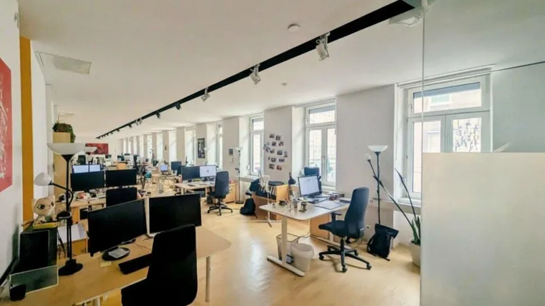 Großes, helles Großraumbüro mit vielen Arbeitsplätzen, Holzboden und natürlichem Licht.
