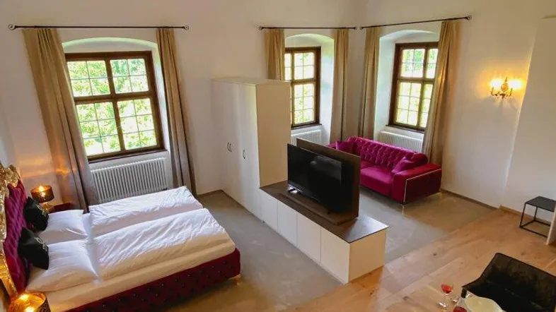 Geräumiges Schlafzimmer mit hohen Decken, Holzboden, einem bequemen Bett, Sofa und Essbereich.