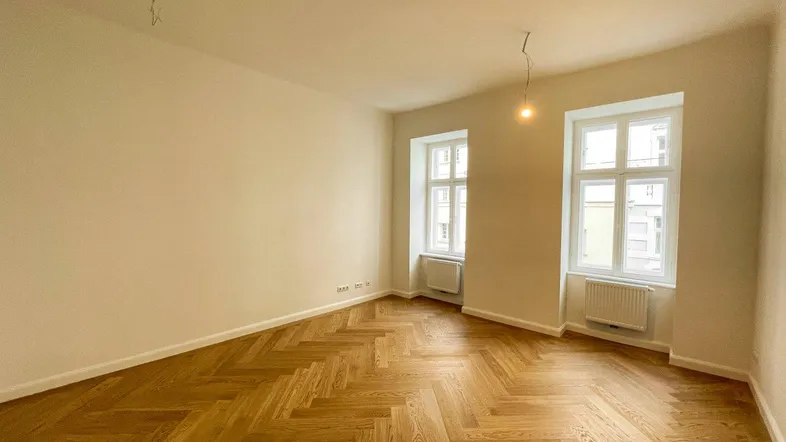 Helles Zimmer mit Fischgrätparkettboden und zwei Fenstern, bereit zur individuellen Gestaltung.