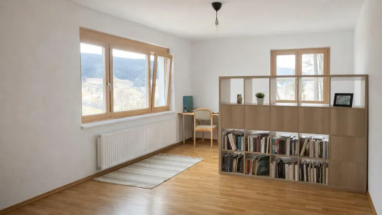 Helles Zimmer mit Holzboden, großem Fenster und Bücherregal, ideal als Wohn- oder Arbeitsbereich.