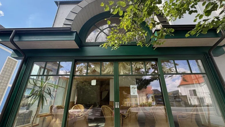 Außenansicht eines Wintergartens mit großen Glasfronten und einem dekorativen Bogenfenster im oberen Bereich.