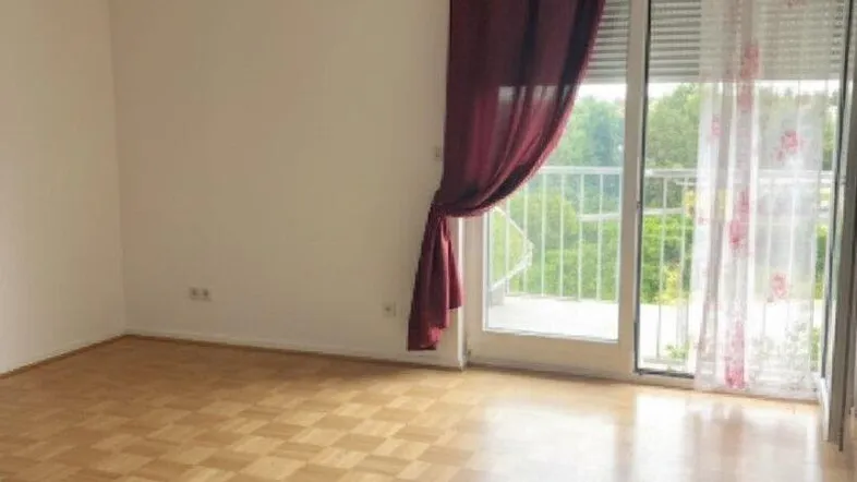 Helles Zimmer mit Parkettboden und Zugang zu einem Balkon, bietet einen grünen Ausblick.