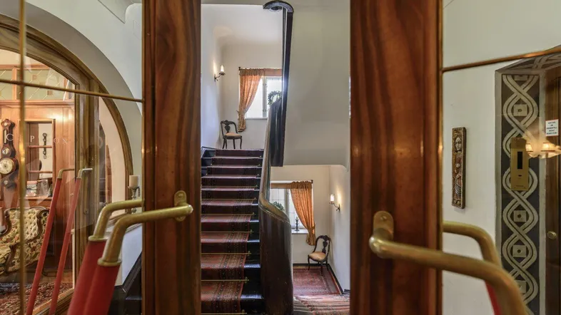 Eindrucksvolles Treppenhaus mit eleganten Holzgeländern, rotem Teppichläufer und Zugang zu einem Aufzug.