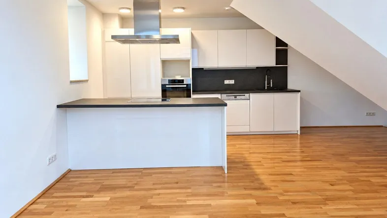 Moderne Küche mit weißer Hochglanzfront, dunkler Arbeitsplatte, Holzboden und Dachschräge.
