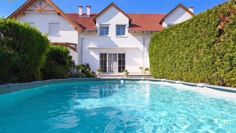 Gepflegter Gartenbereich mit einem Swimmingpool und hoher Hecke hinter dem Haus.