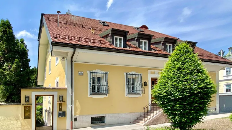 Historisches Gebäude mit gelber Fassade, rotem Ziegeldach und schmiedeeisernen Fenstergittern.