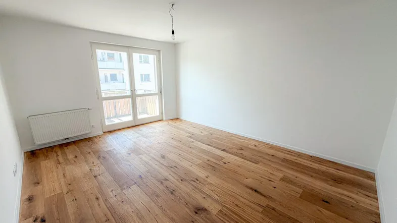 Helles Zimmer mit Holzboden und Zugang zum Balkon, ideal als Wohn- oder Schlafzimmer.