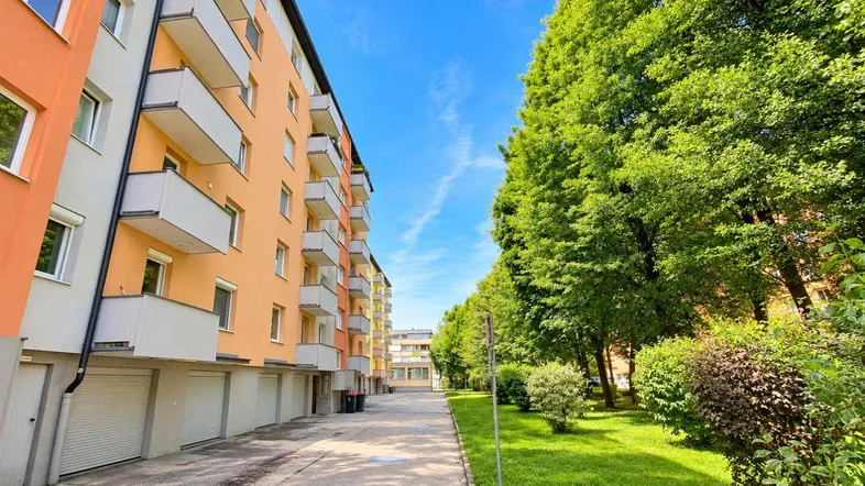 Mehrfamilienhaus mit Balkonen und Garagen, umgeben von viel Grün und Bäumen.