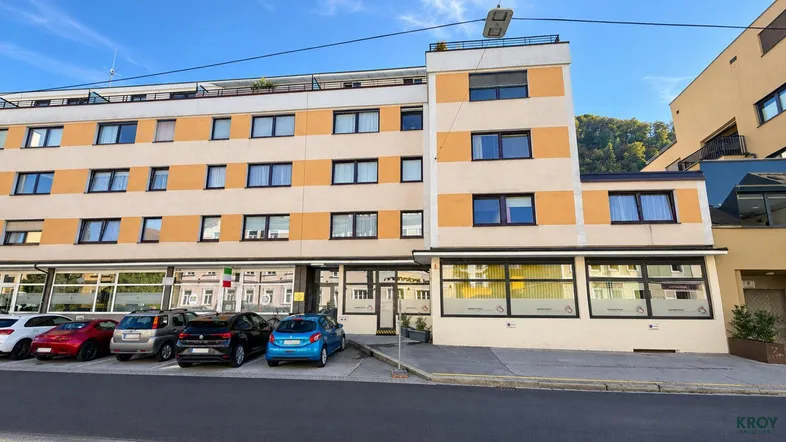 Mehrstöckiges Wohngebäude mit orangefarbenen Akzenten, Flachdach und Parkplätzen davor.
