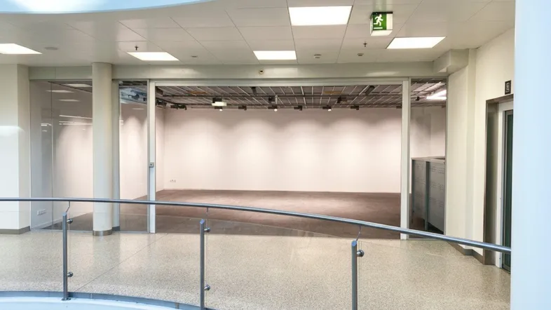 Geräumiger, leerer Gewerberaum mit hohen Decken und großen Glasfronten, gesehen von einem oberen Flur.