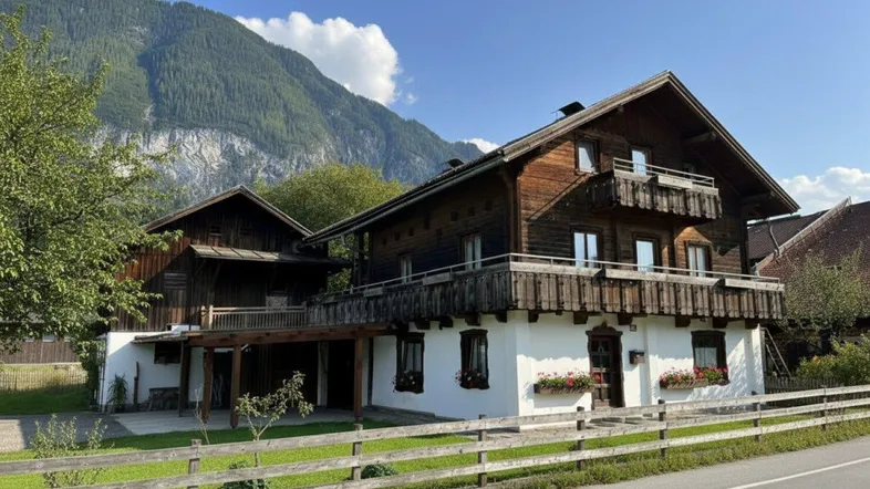 Traditionelles Holzhaus im Chalet-Stil mit Balkonen und beeindruckendem Bergblick unter blauem Himmel.