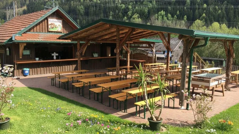 Gemütlicher Außenbereich mit Holztischen und Bänken unter einer Überdachung, umgeben von grüner Natur und Bergen.