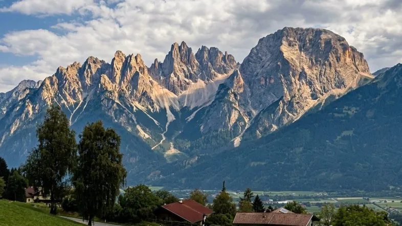 Panoramablick auf majestätische Berge und ein grünes Tal mit vereinzelten Häusern.